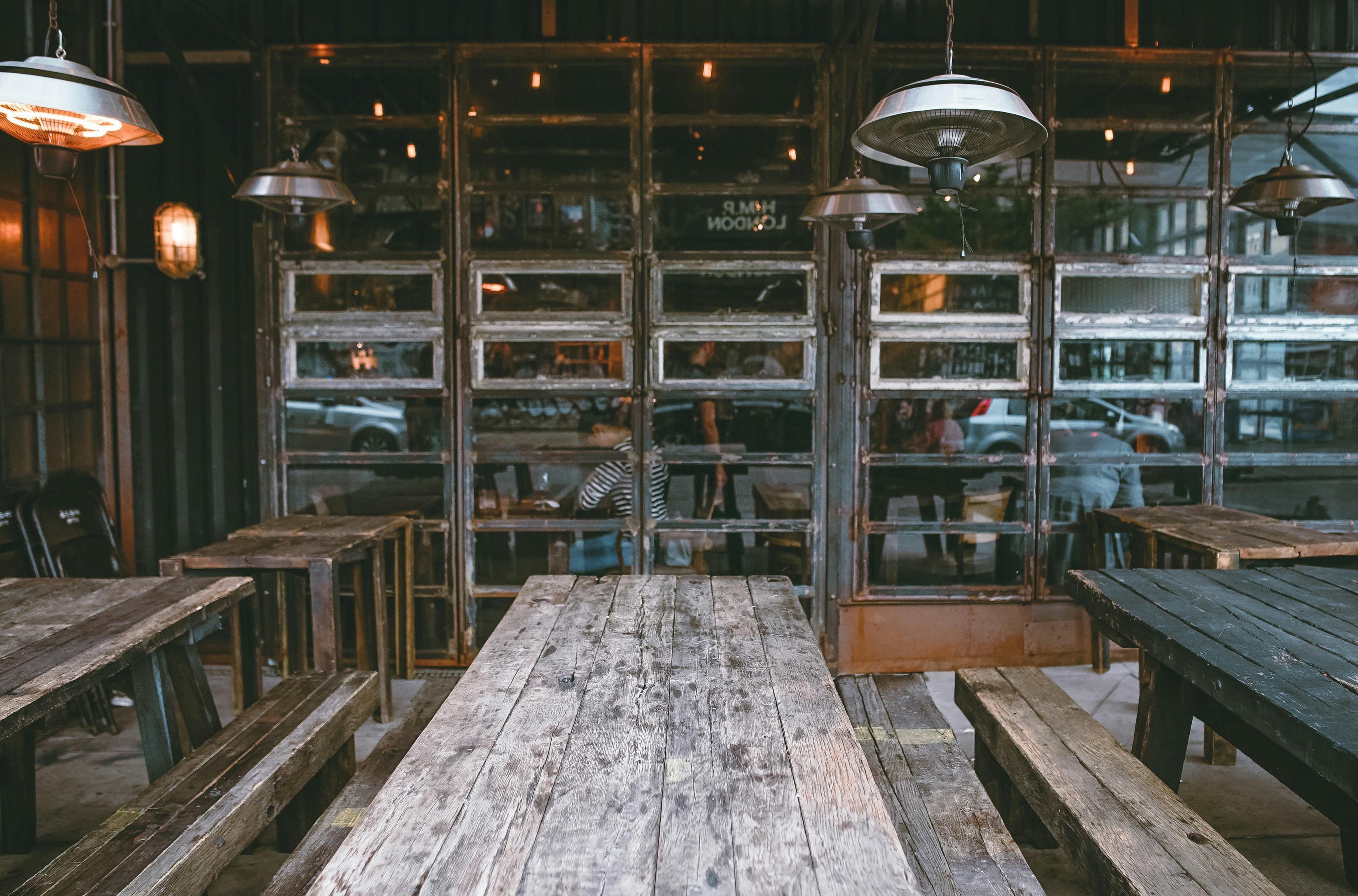 Weathered wooden tables beneath hanging heaters in a rustic restaurant dining area.